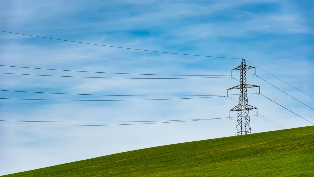 An electricity pylon on a green hillside under a blue sky